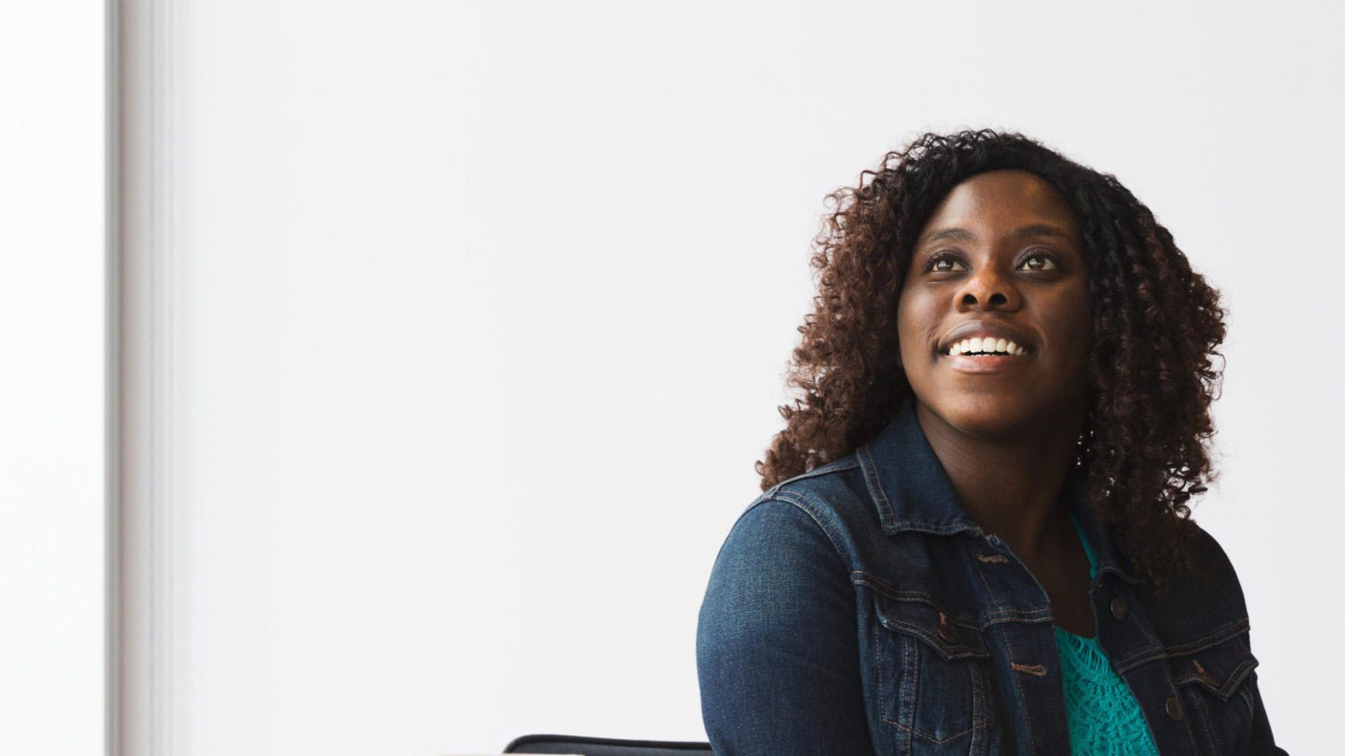 Young woman sitting in front of a white wall, smiling.