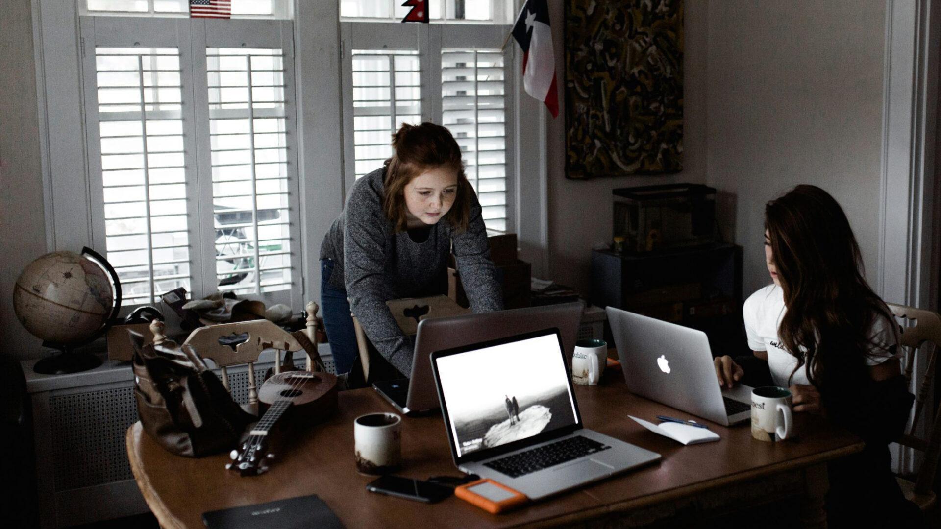 Two students working on laptops at a table.