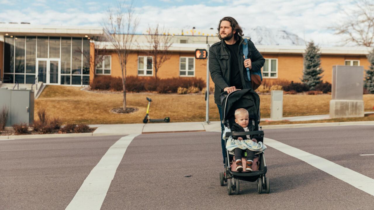 young father with backpack pushes child in stroller while crossing the street