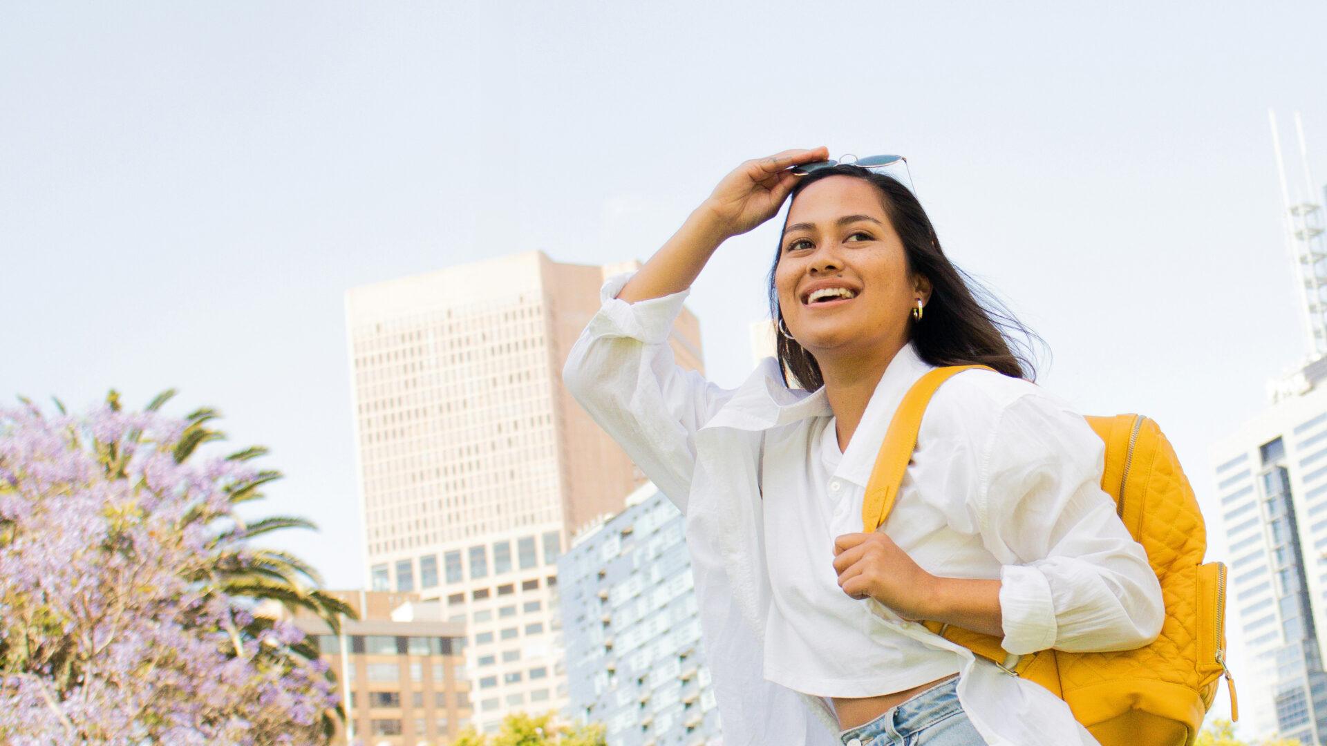 Happy student with backpack walking through city campus.