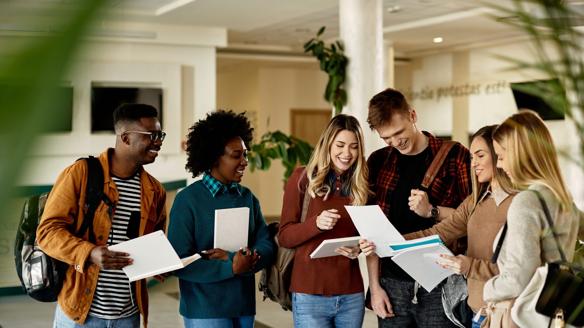 Group of happy students looking at exam results while standing at university hallway.