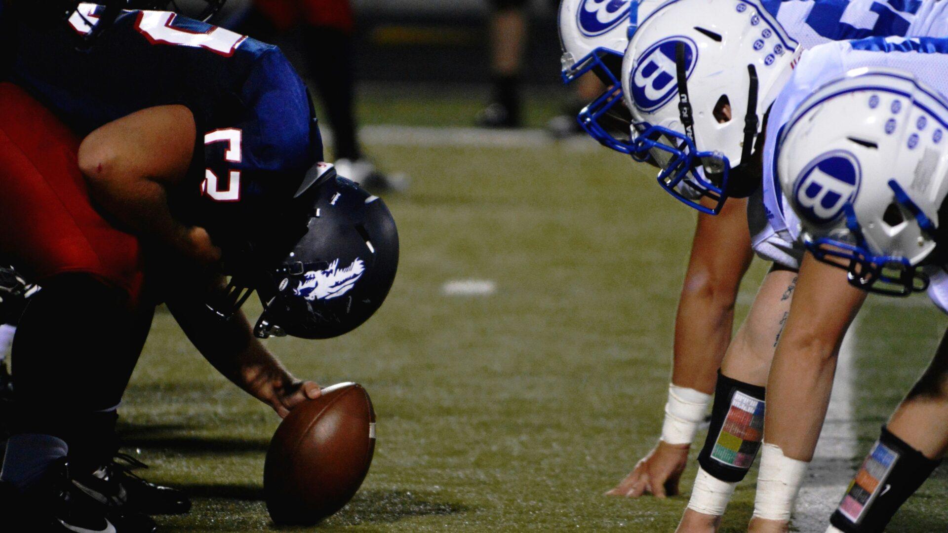American football players in two teams wearing blue and white uniforms at a lineup on an American football field