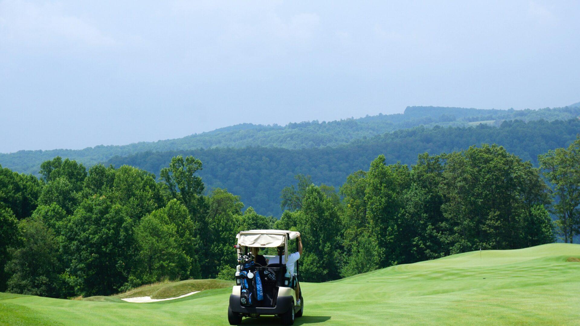Landscape of a gold course with a golf cart in the center and a blue sky above mountains in the background