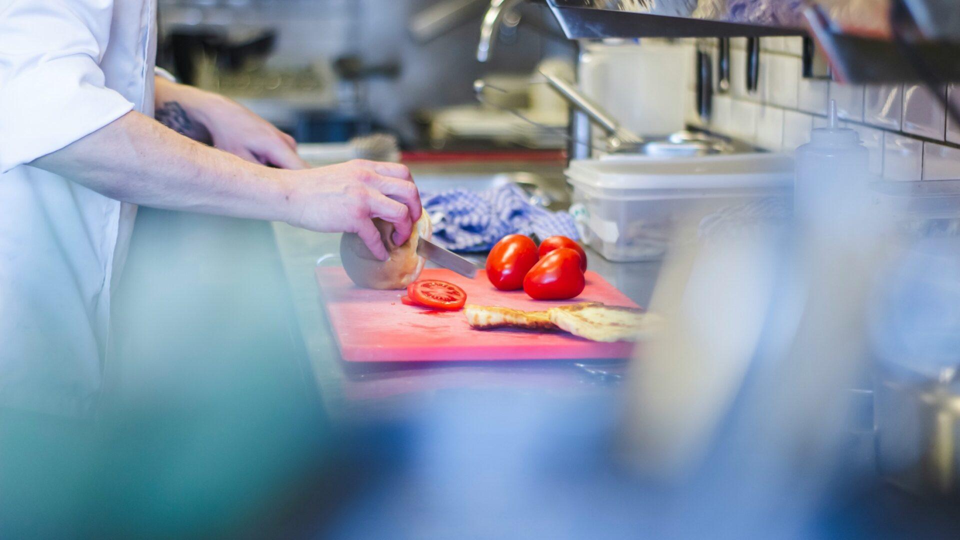 Culinary student in a kitchen using a red cutting board to chop tomatoes