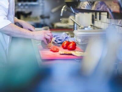 Culinary student in a kitchen using a red cutting board to chop tomatoes