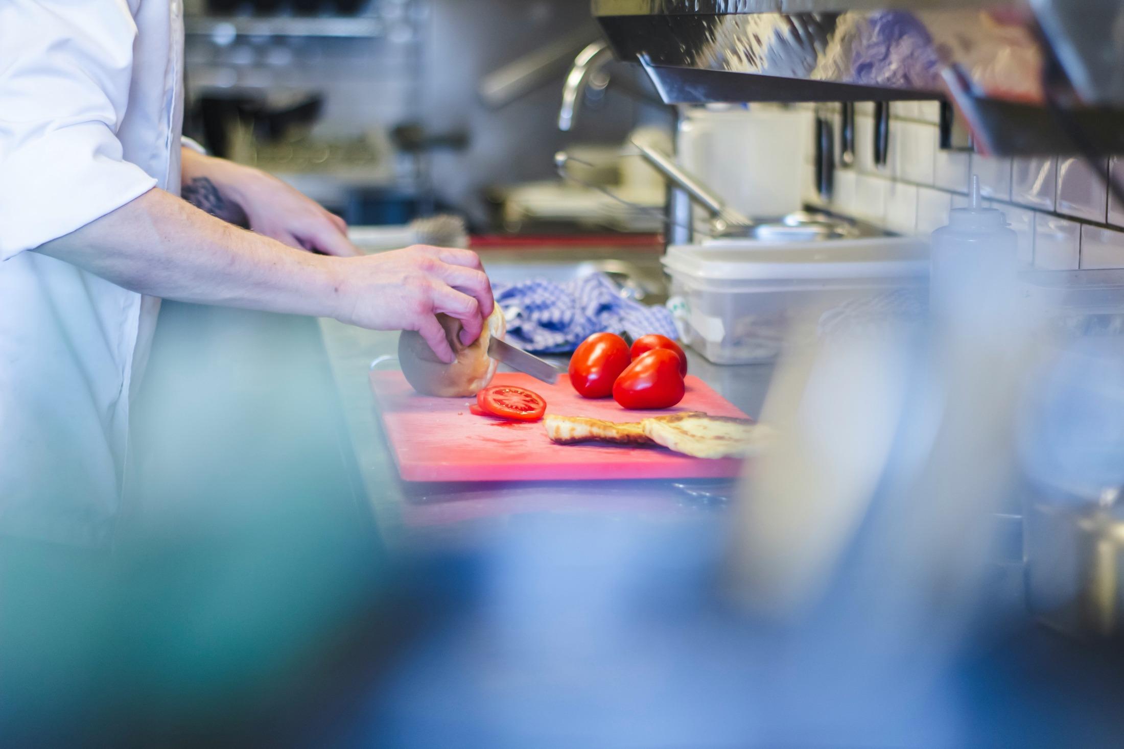 Culinary student in a kitchen using a red cutting board to chop tomatoes