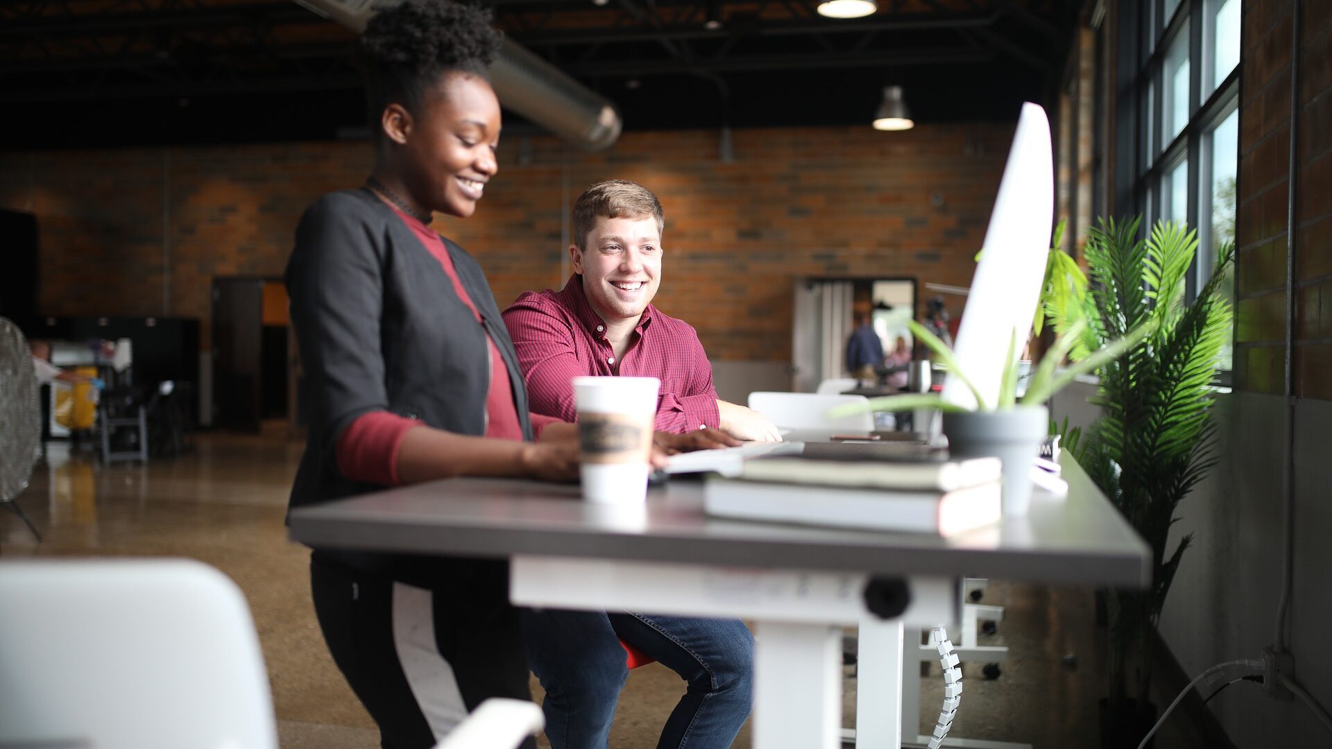 Two people sitting at a computer desk in a workplace.