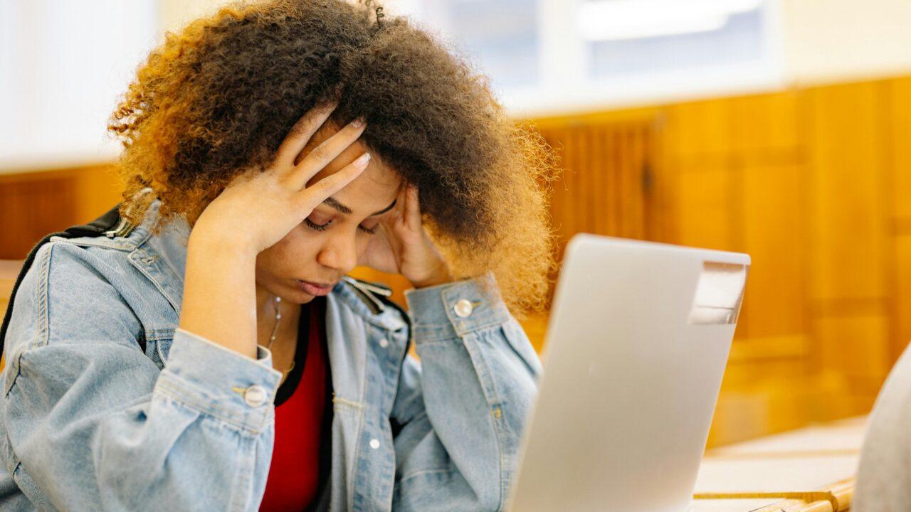 A student in front of a laptop holding her head in frustration.