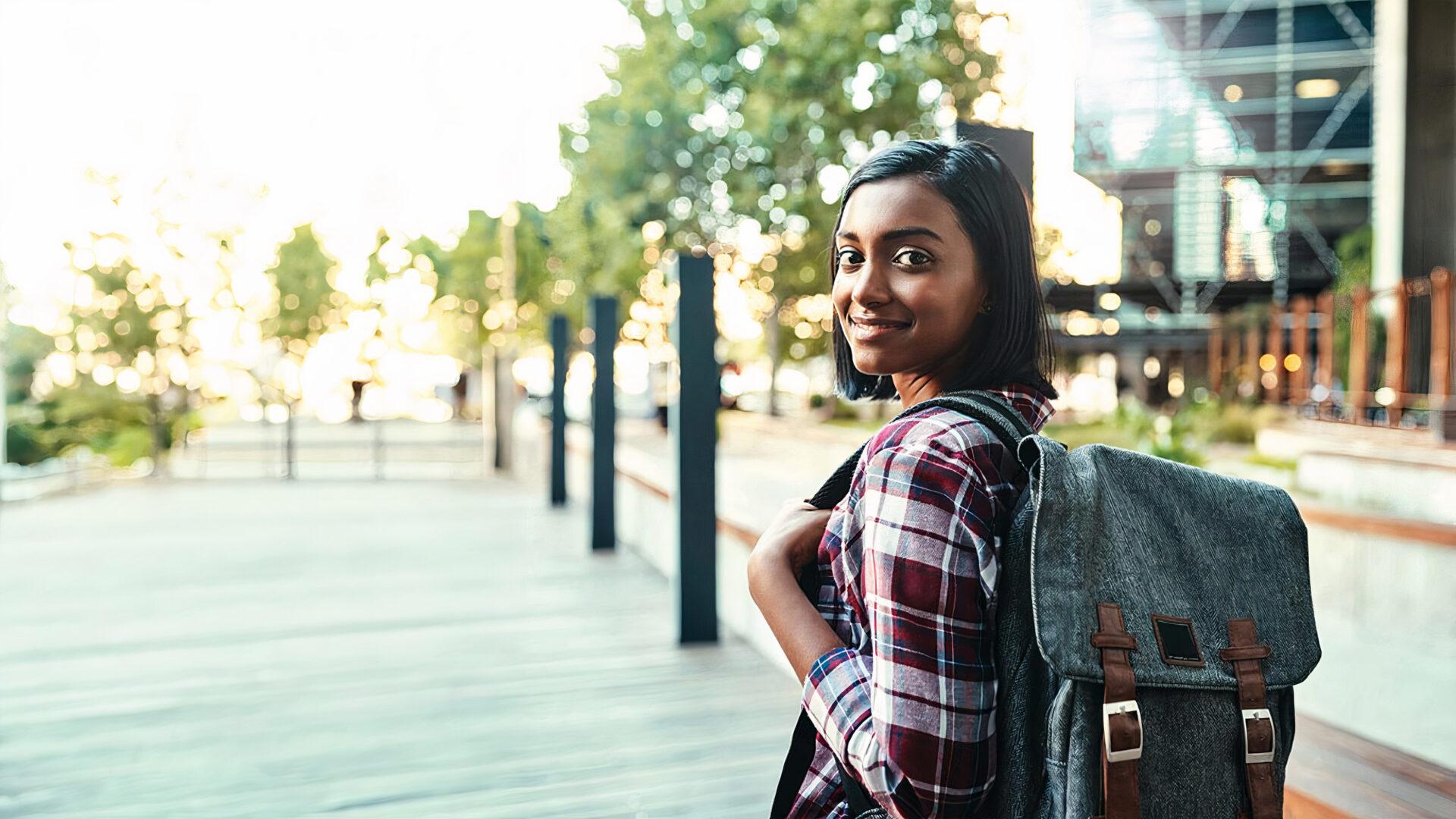 A young woman with a backpack looks over her shoulder at the camera as she walks down the path.