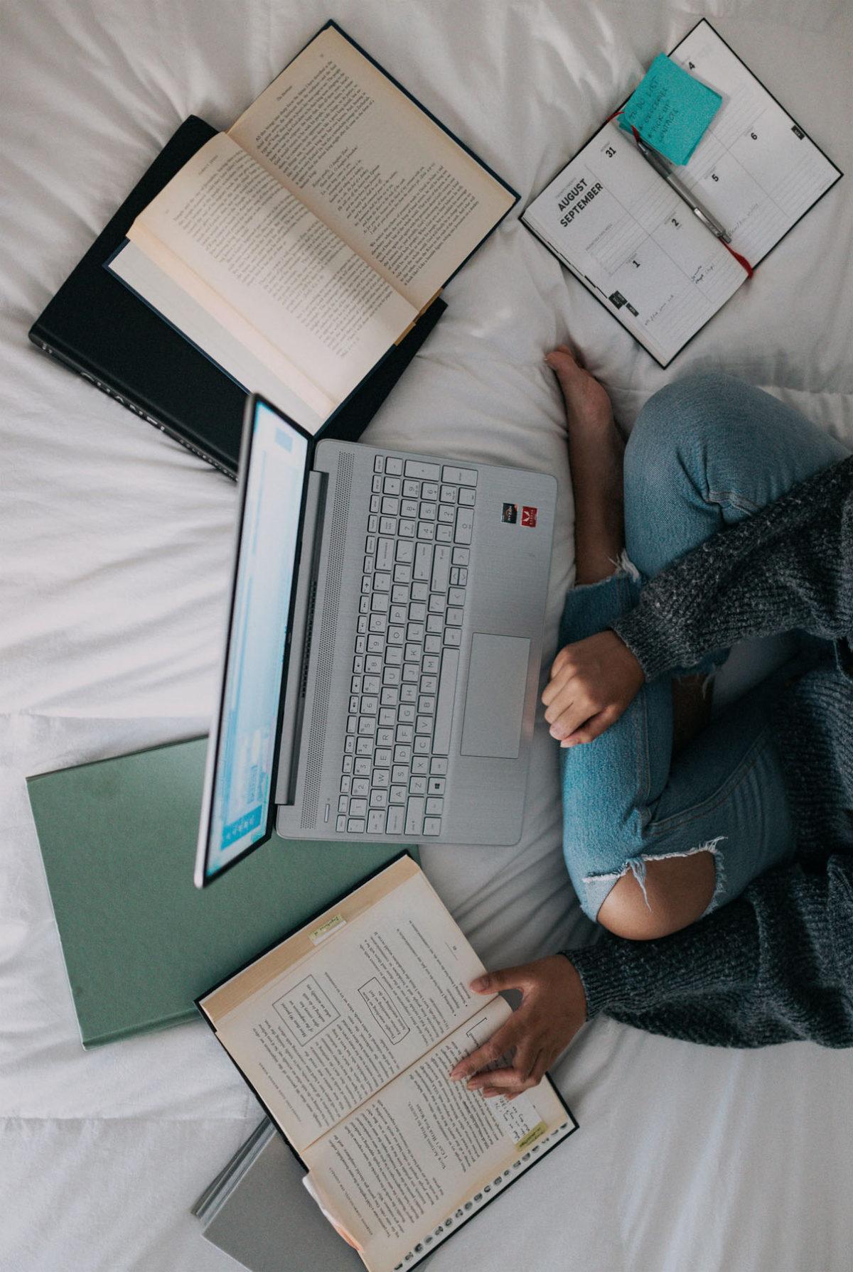 student studying on laptop surrounded by textbooks