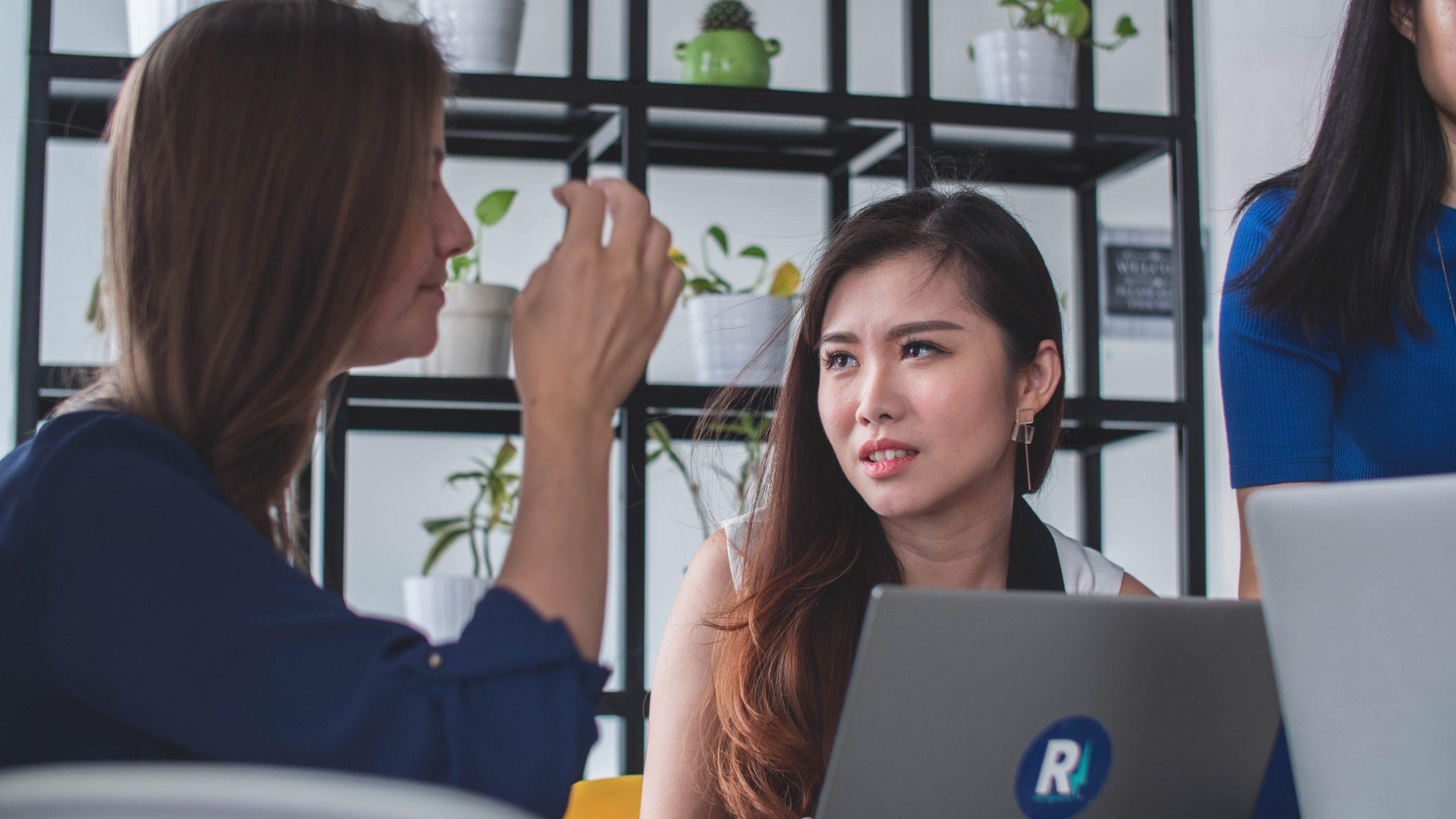 Two people talking while working on a laptop.