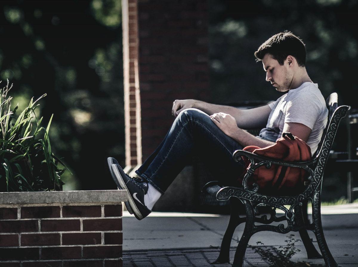 young male student reading a book on a bench outside