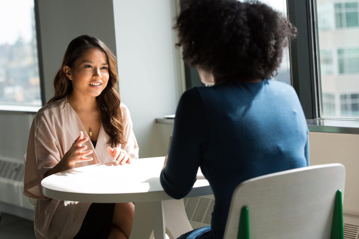 Two young women talking to one another across a table.