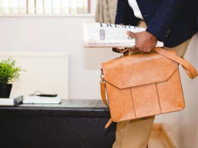 man holding brown leather bag and business section of newspaper