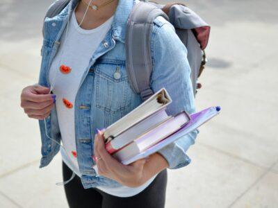 woman wearing a blue denim jacket and gray backpack and carrying school books