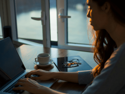 woman in low light sits at a laptop with a cup of coffee