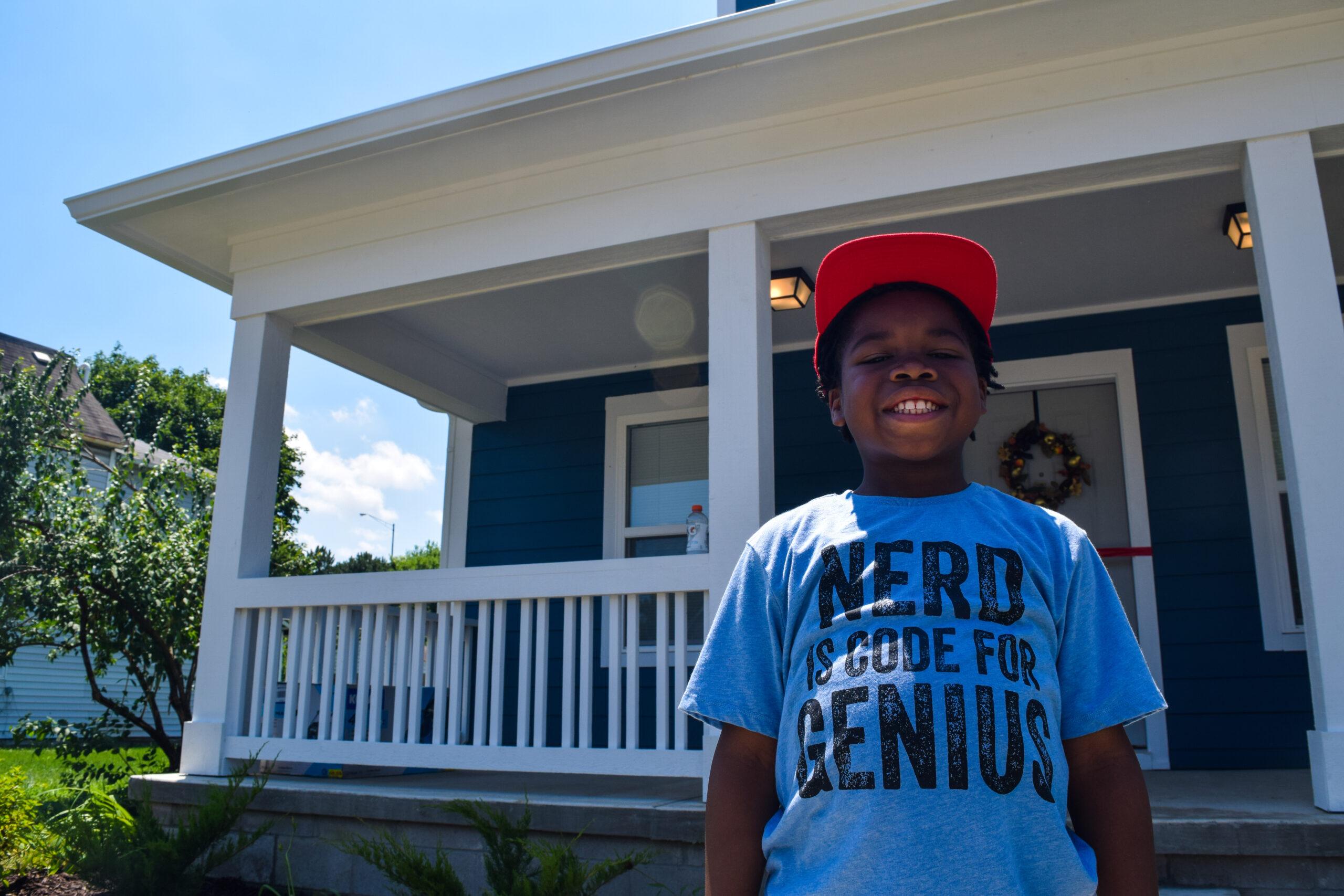 A young boy smiles outside his new home provided by Habitat for Humanity