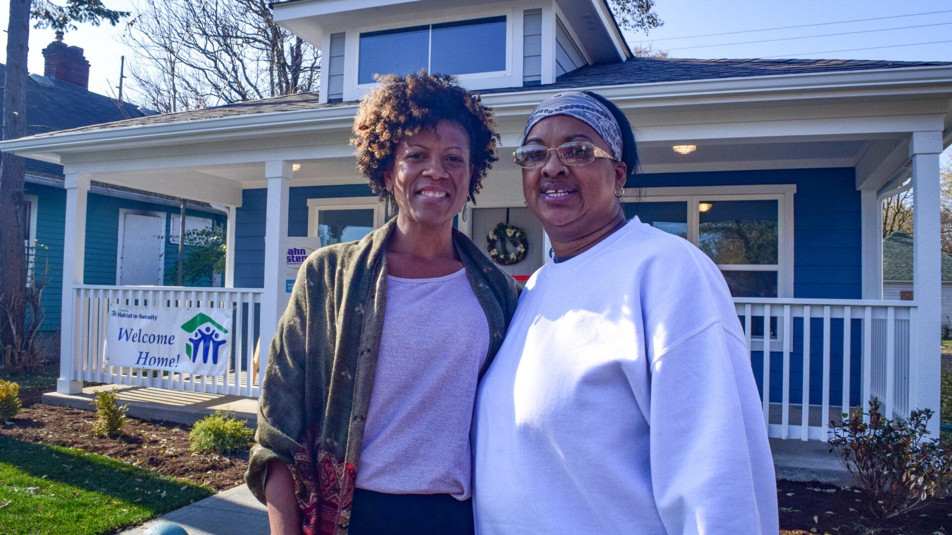 Two women stand outside their new home built by Habitat for Humanity