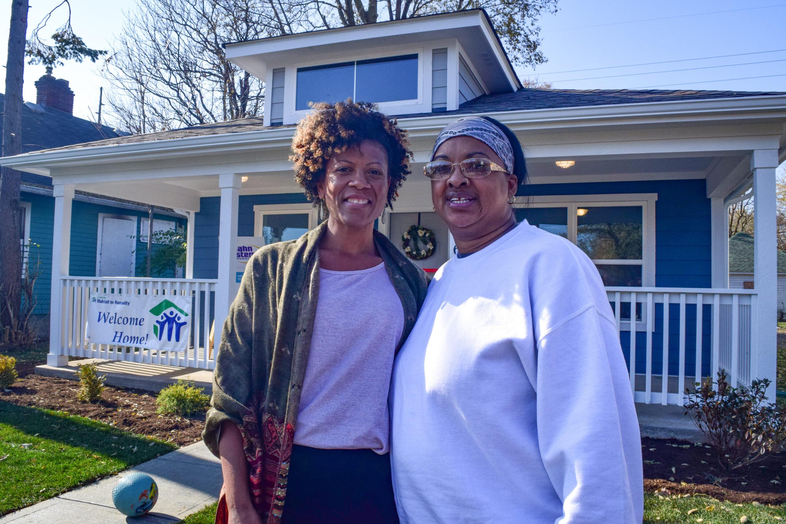 Two women stand outside their new home built by Habitat for Humanity