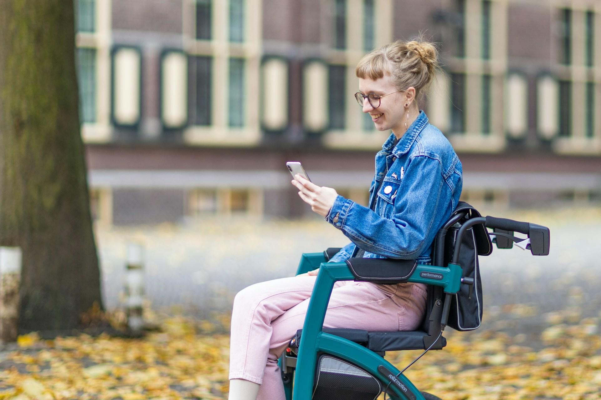 A woman sitting in an electric mobility chair and using a cell phone on a college campus