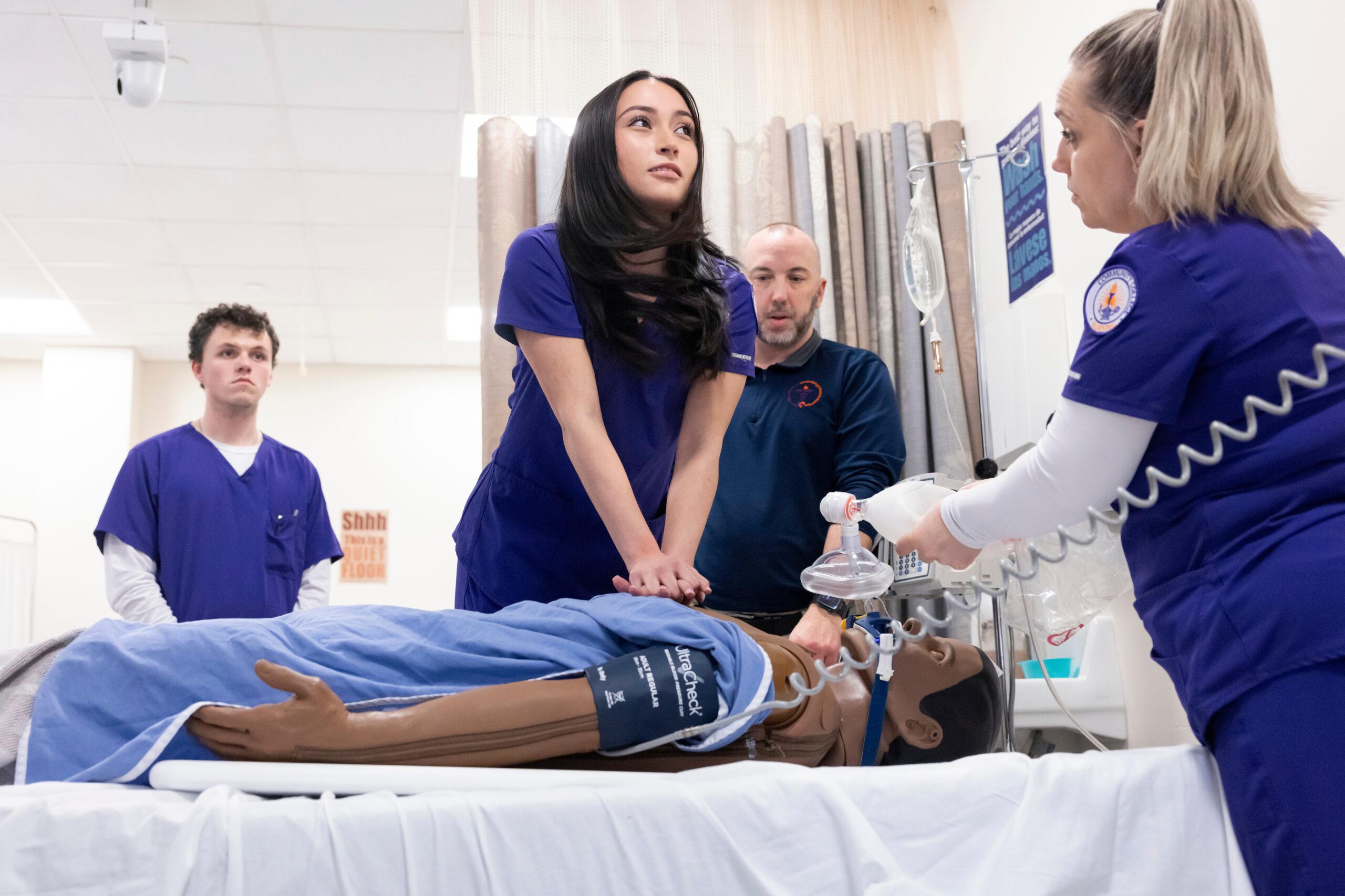 Female nursing student giving chest compressions during a CPR lesson in a lab classroom on a college campus.