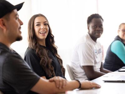 Hispanic female student smiling at fellow students during a class in a sunny classroom on a college campus.