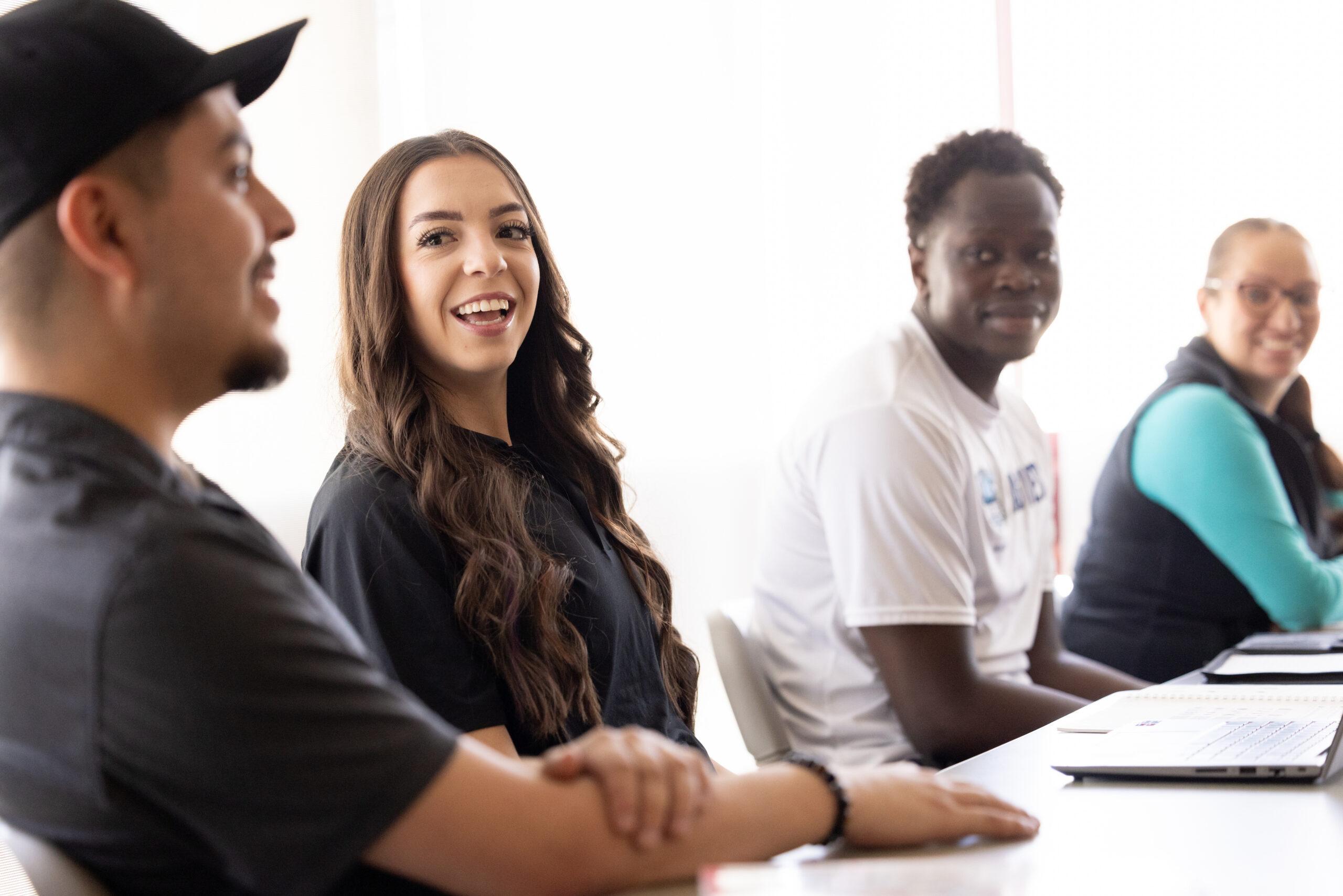 Hispanic female student smiling at fellow students during a class in a sunny classroom on a college campus.