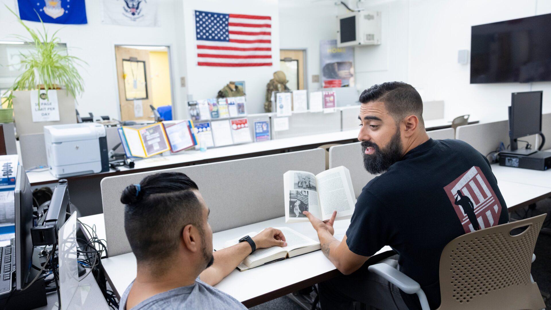 male veteran staff member tutoring a male student veteran in a veterans resource center on a college campus.