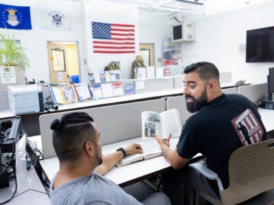 male veteran staff member tutoring a male student veteran in a veterans resource center on a college campus.