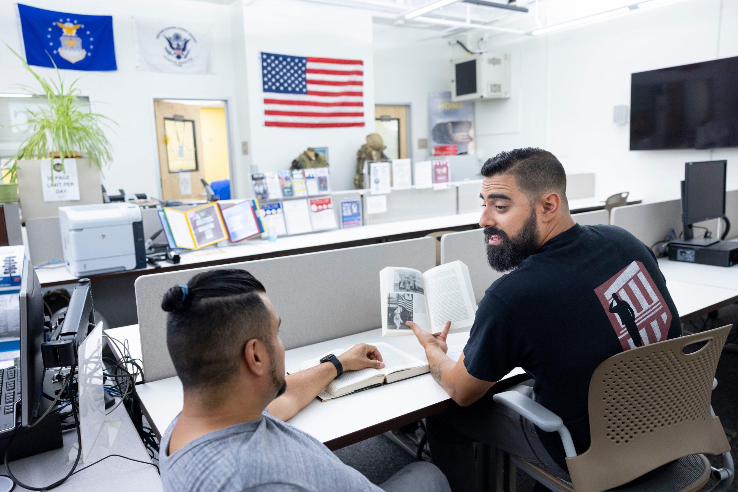 male veteran staff member tutoring a male student veteran in a veterans resource center on a college campus.