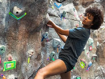 A photo of a Black college-aged woman rock climbing. She is kyla, a scholarship recipient